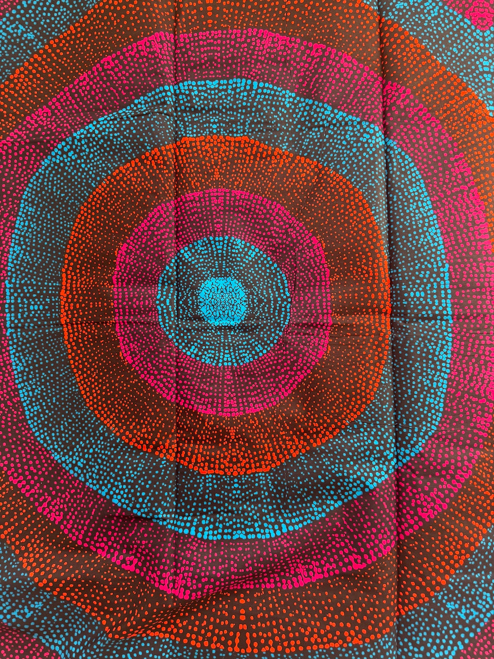 Close-up of a fabric with concentric circular pattern in red, blue, and orange.