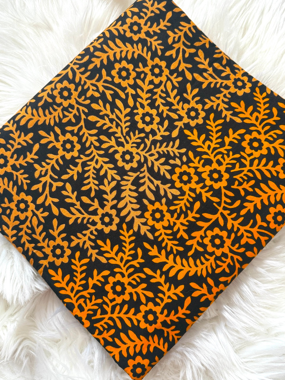 Black fabric with orange floral pattern on a white fluffy surface