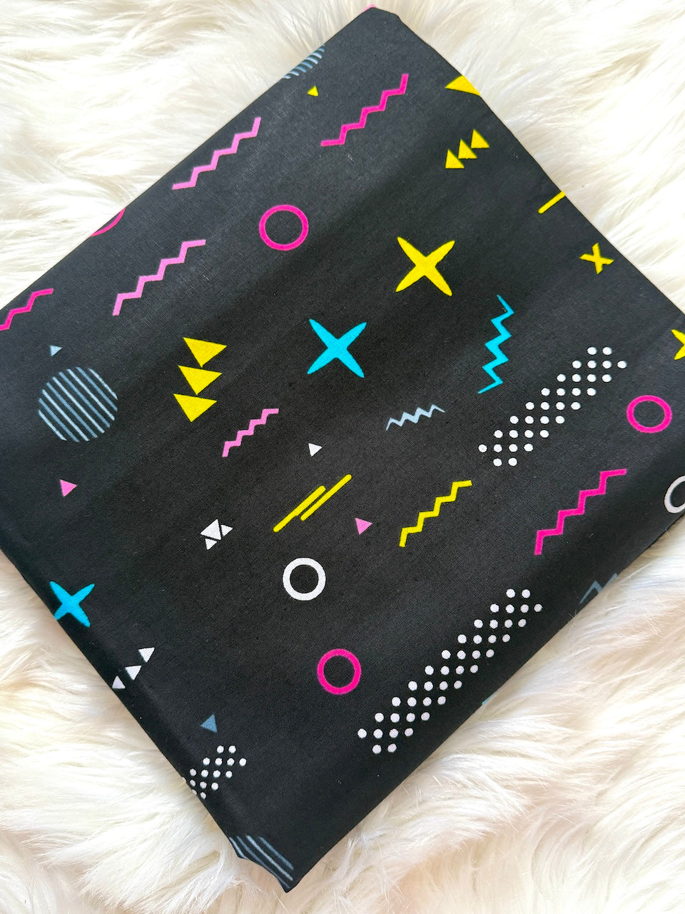 Black fabric with colorful geometric patterns on a white fluffy surface