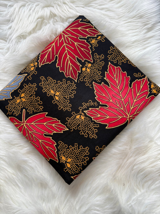 Fabric with red maple leaf pattern on a black background, laid flat on a white textured surface.
