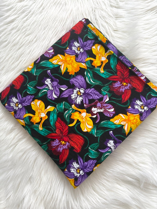 Floral-patterned fabric with red, yellow, and purple flowers on a black background, placed on a white fluffy surface.