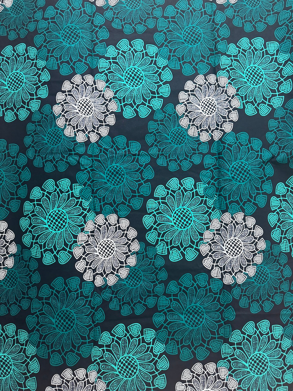 Pattern of lace-like flowers in teal and white on a dark background