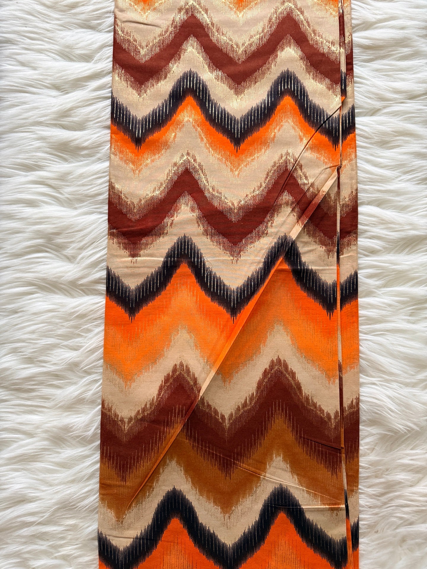Chevron patterned fabric with orange, brown, and black colors on a white textured background