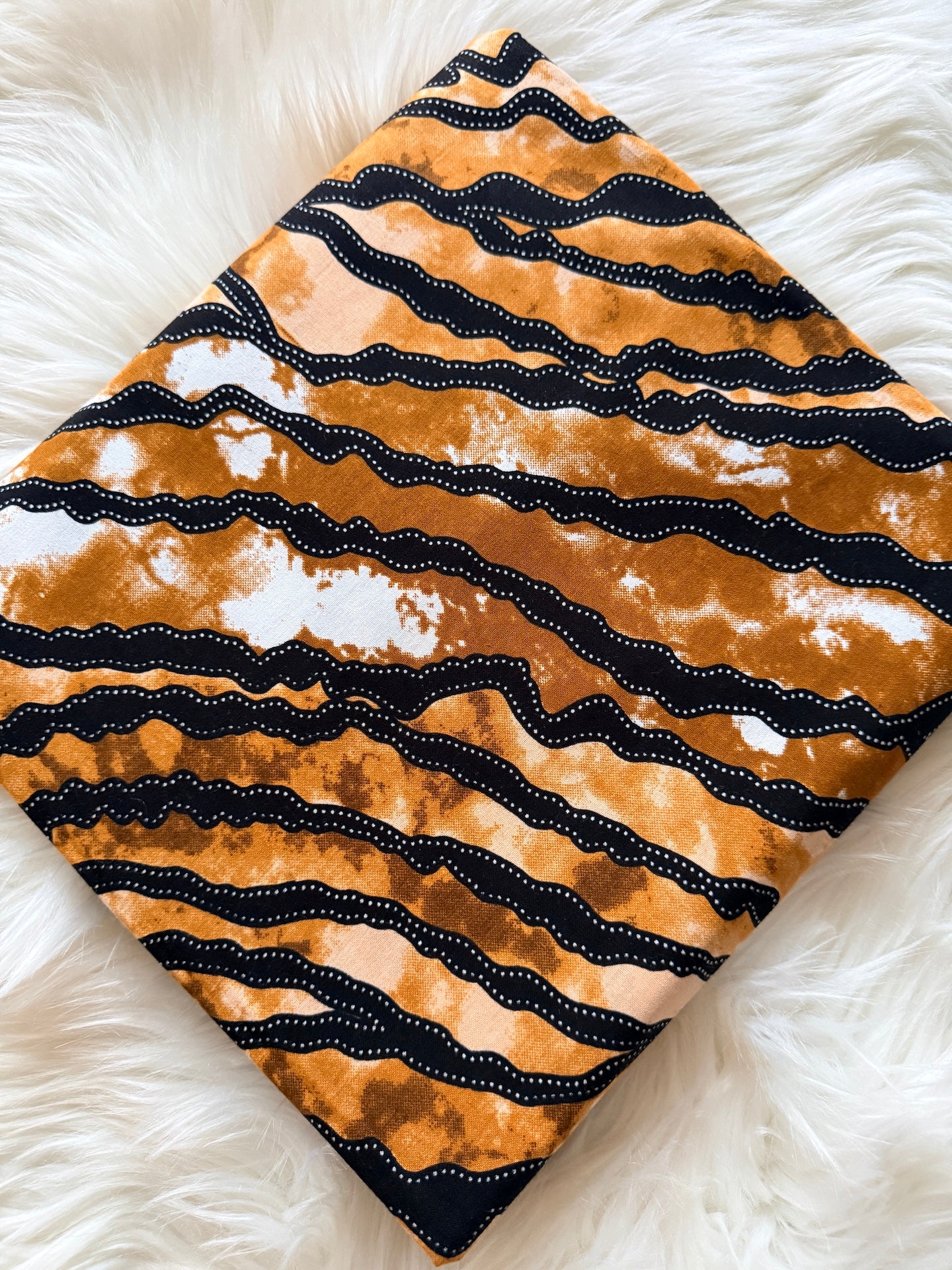 Fabric with black wavy pattern on a beige background, placed on a white fluffy surface.