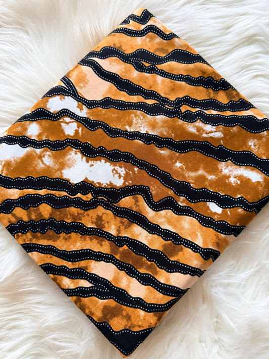 Fabric with black wavy pattern on a beige background, placed on a white fluffy surface.