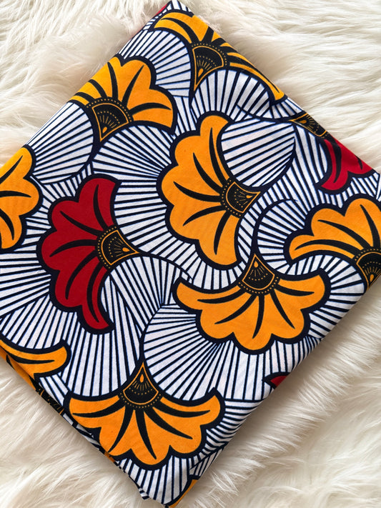 African print fabric with orange, black, and red patterns on a white fluffy surface