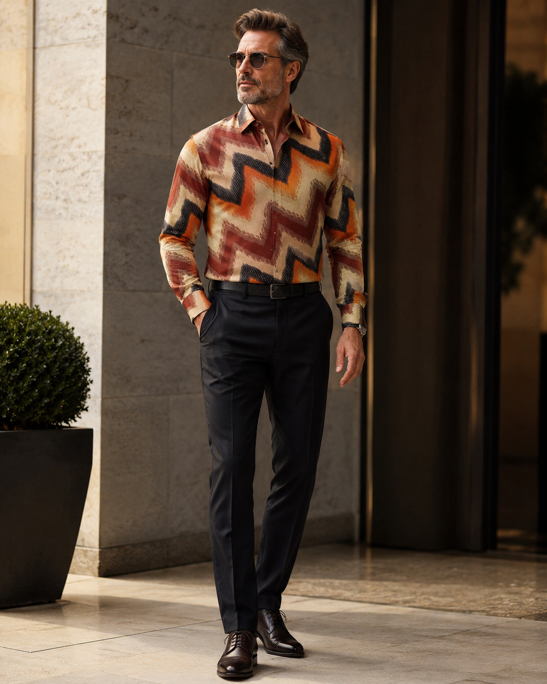 Man wearing a patterned shirt and dark pants standing in an urban setting.
